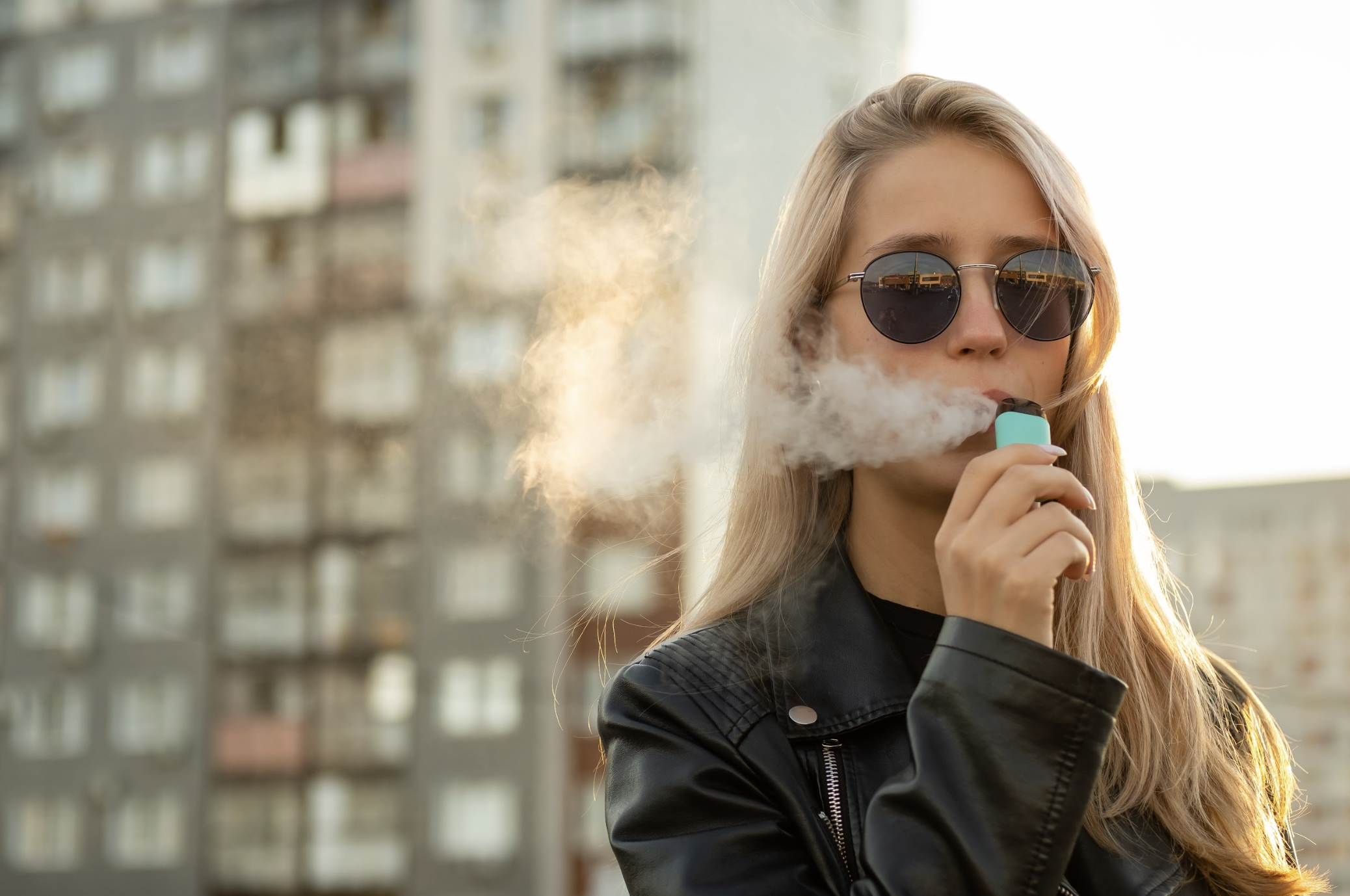 Woman vaping in front of city buildings. 